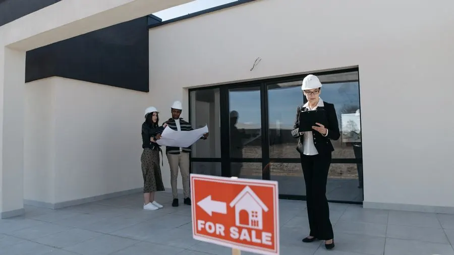 Real estate agents in hard hats reviewing plans beside a house for sale.